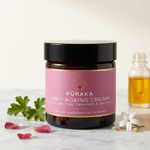 Pūraka Anti-Ageing Cream with Rose Absolute, Geranium and Jasmine on marble surface with geranium leaves, rose petals and jasmine flowers